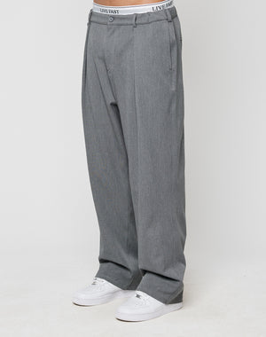 Someone wears LIVE FAST DIE YOUNG Wide Casual Pants in gray with an elastic waistband, styled with white sneakers. The LIVE FAST underwear waistband is visible above the straight-leg pants against a plain white background.