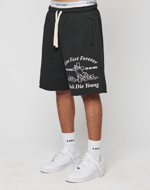 A person wears LFDY Praying Shorts by LIVE FAST DIE YOUNGāregular fit, black with white āLive Fast Forever, Fuck Die Youngā text and rose graphic, elastic waistband, side pocketsāpaired with āLDYā socks and white sneakers.