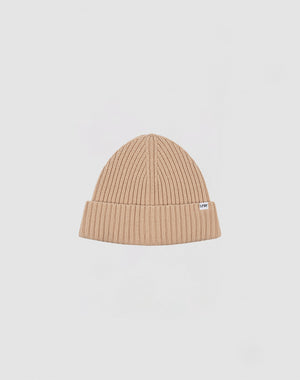 A beige Washed Rib Knit Beanie von LIVE FAST DIE YOUNG aus Baumwolle mit umgeschlagenem Rand und kleinem weißem Etikett an der Seite vor schlicht hellgrauem Hintergrund.