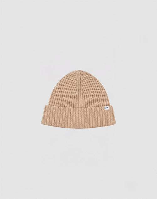 A beige Washed Rib Knit Beanie von LIVE FAST DIE YOUNG aus Baumwolle mit umgeschlagenem Rand und kleinem weißem Etikett an der Seite vor schlicht hellgrauem Hintergrund.