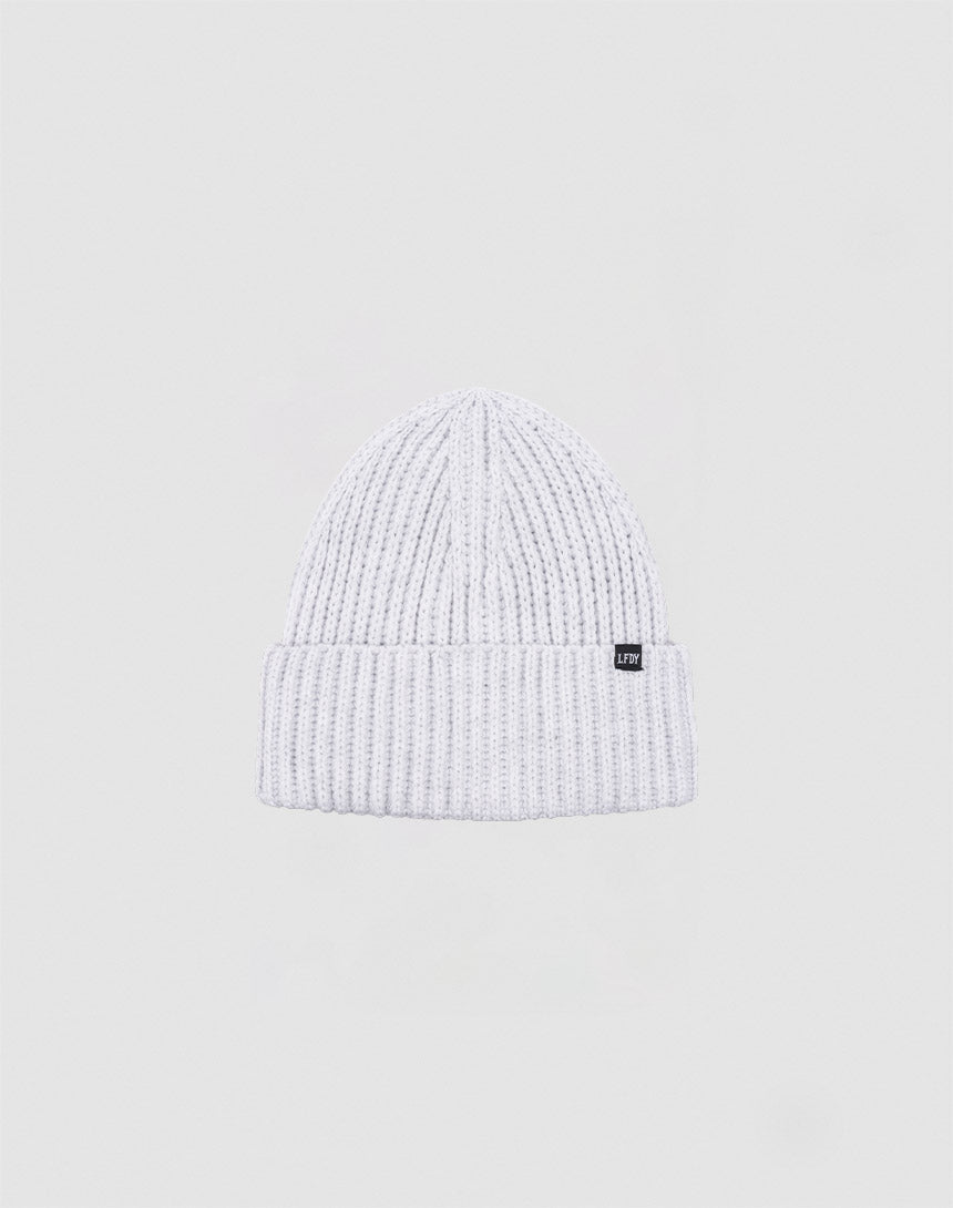 The LIVE FAST DIE YOUNG Rib Knit Beanie, made from soft acrylic with a folded brim and a small black front label, is displayed against a plain light gray background.