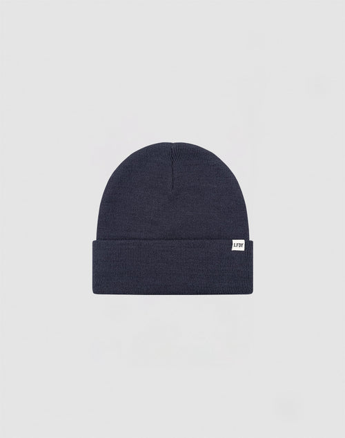The LIVE FAST DIE YOUNG Basic Beanie is a plain dark navy blue knit, One Size, with a folded brim and a small white Flaglabel tag on the front, displayed against a light gray background.