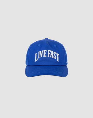 The Live Fast Unstructured Cap by LIVE FAST DIE YOUNG is a blue baseball cap with LIVE FAST in bold white letters on the front and a Flag-Label on the side, displayed against a plain light gray background.