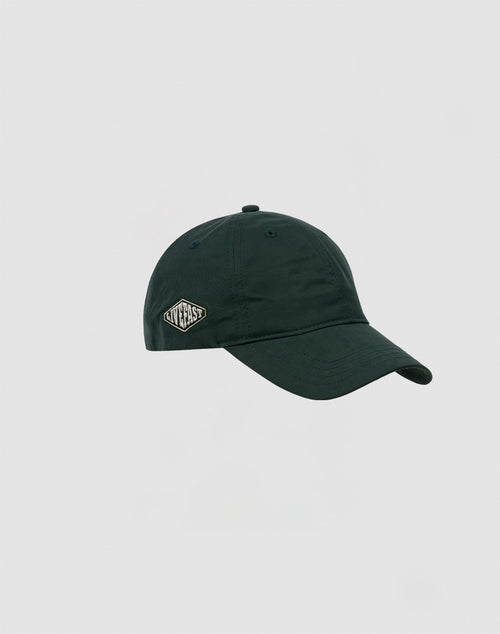 The Basic Cap by LIVE FAST DIE YOUNG is a dark green polyester baseball cap with a curved brim, a small white NEW FAST embroidered patch, and an adjustable Klettverschluss, shown on a plain light gray background.