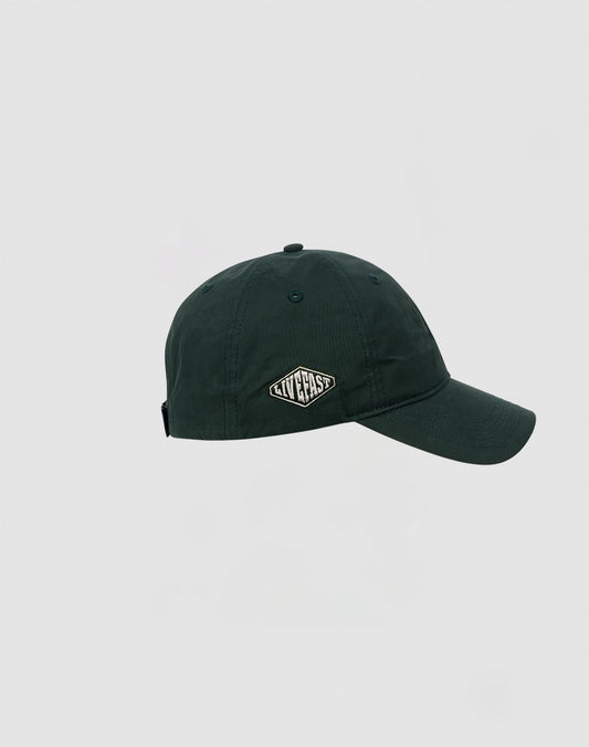 A dark green Basic Cap by LIVE FAST DIE YOUNG made of polyester with a curved brim and a small oval patch on the front displaying the brand name in white letters. Shown against a plain light gray background.