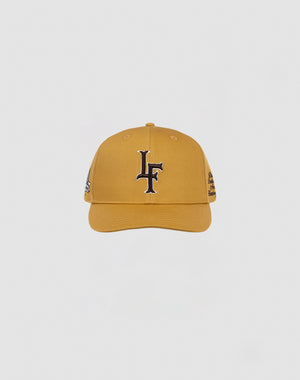 The LF 10th Snapback by LIVE FAST DIE YOUNG is a mustard yellow cotton baseball cap with a black and white LF logo on the front and a snap closure, shown against a plain white background.