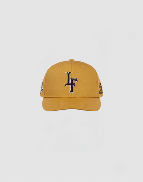 The LF 10th Snapback by LIVE FAST DIE YOUNG is a mustard yellow cotton baseball cap with a black and white LF logo on the front and a snap closure, shown against a plain white background.