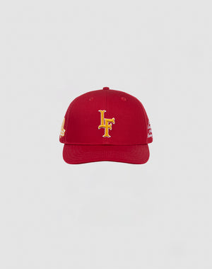 The LIVE FAST DIE YOUNG LF 10th Snapback is a red baseball cap with a yellow embroidered LF logo, made from 100% Baumwolle and designed with a Mit Snapverschluss, shown on a plain light gray background.