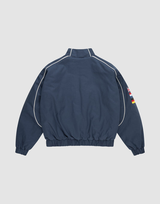 The LFDY Canvas Jacket by LIVE FAST DIE YOUNG is navy blue with white piping, elastic cuffs and waistband, and multicolor flag embroidery on the left sleeve, shown from the back against a plain white background.