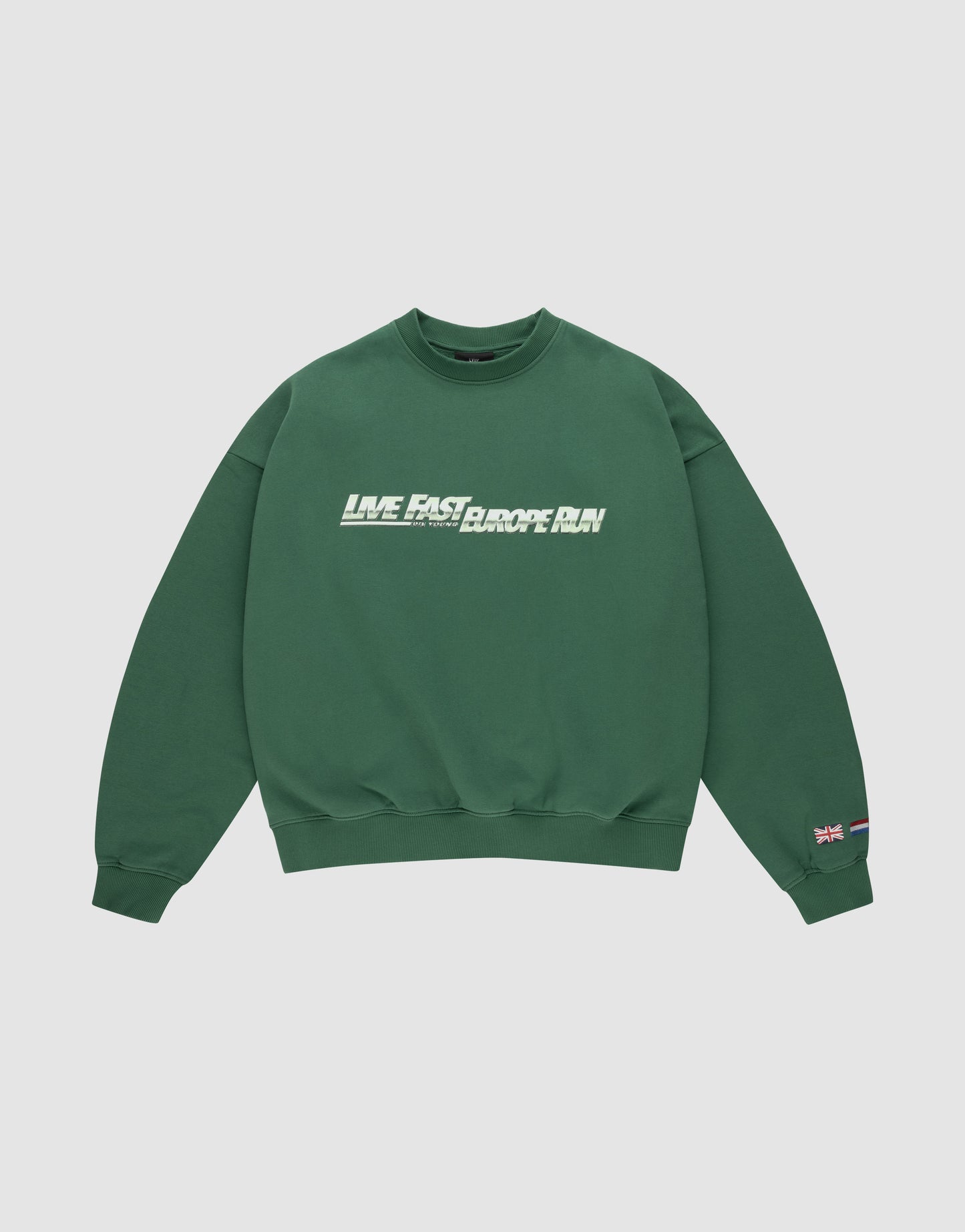 The LFDY Europe Run Sweater by LIVE FAST DIE YOUNG is a forest green oversized crewneck with “LIVE FAST, RACE RUN” in bold white and green front print and small flag patches on the left sleeve near the cuff. Made from soft Baumwolle.