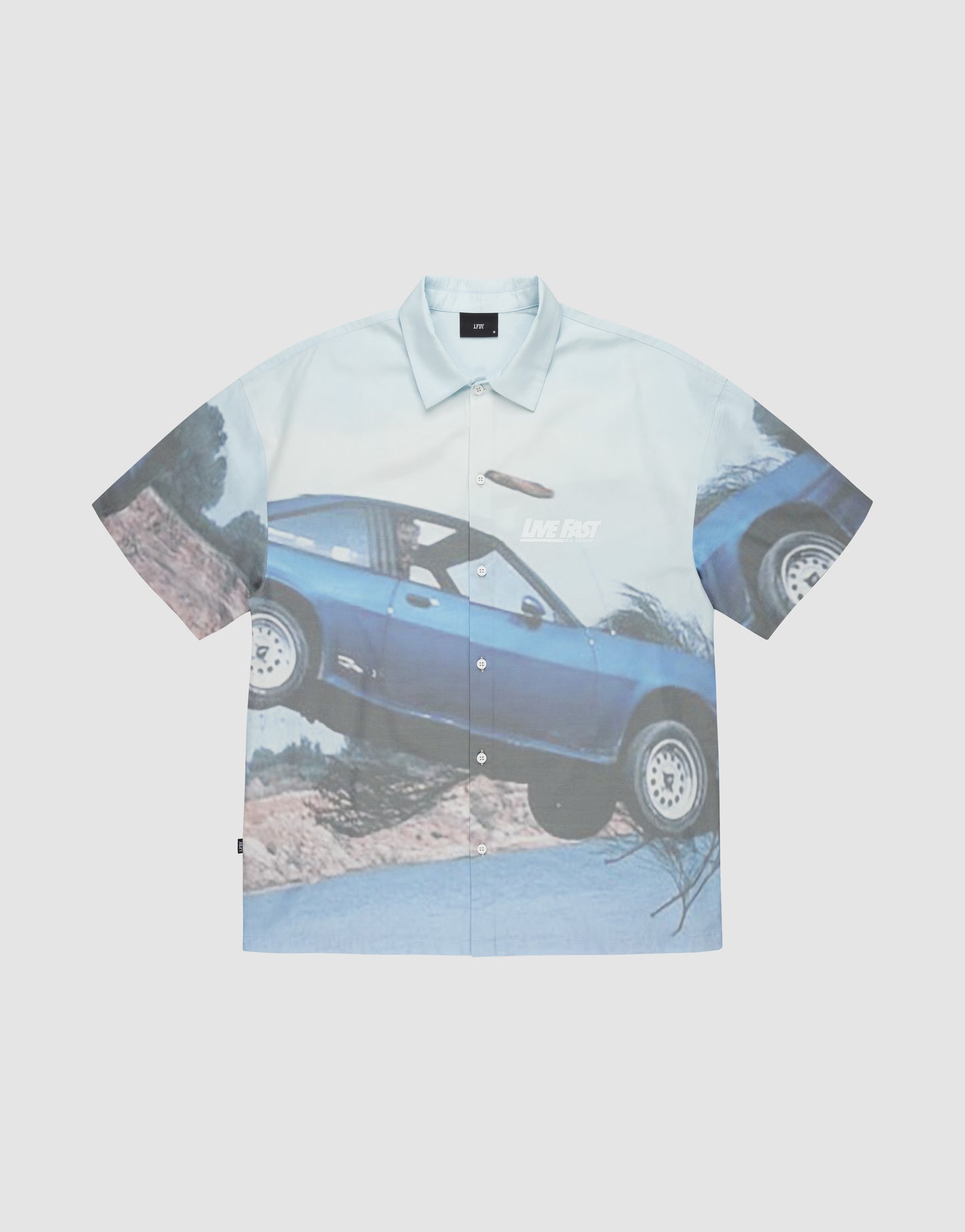 The LFDY Crash Kid Shirt by LIVE FAST DIE YOUNG features short sleeves and an oversized blue car print mid-jump over dirt, with "LIVE FAST" and a bold logo on the car door.