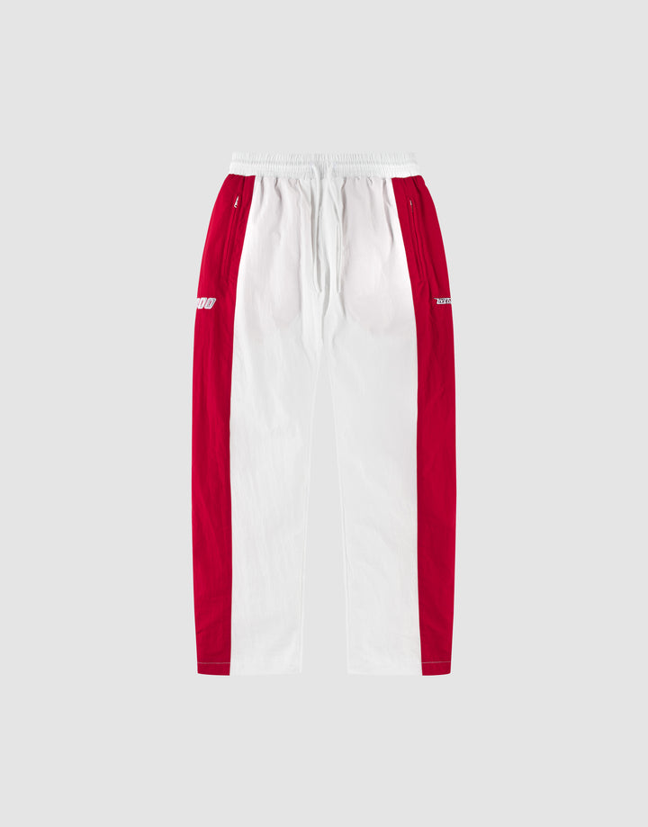 The LIVE FAST DIE YOUNG LFDY Trackpants 3000 are wide fit pants with a white center, red side panels, an elastic waistband, and small white logos on the red hip sections, shown against a light gray background. | plain