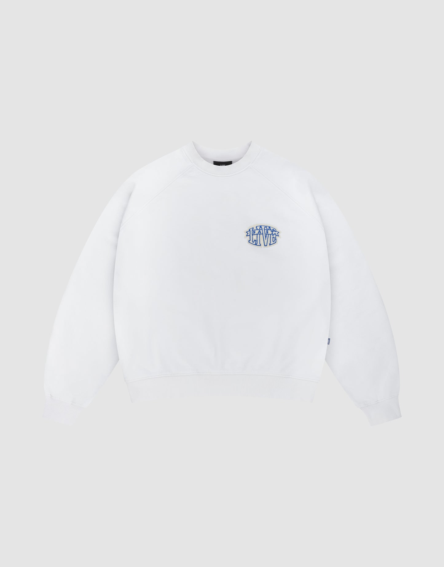 The LFDY Radiator Sweater by LIVE FAST DIE YOUNG is an oversized white crewneck featuring a small blue and yellow graphic text on the left chest, shown against a light grey background.