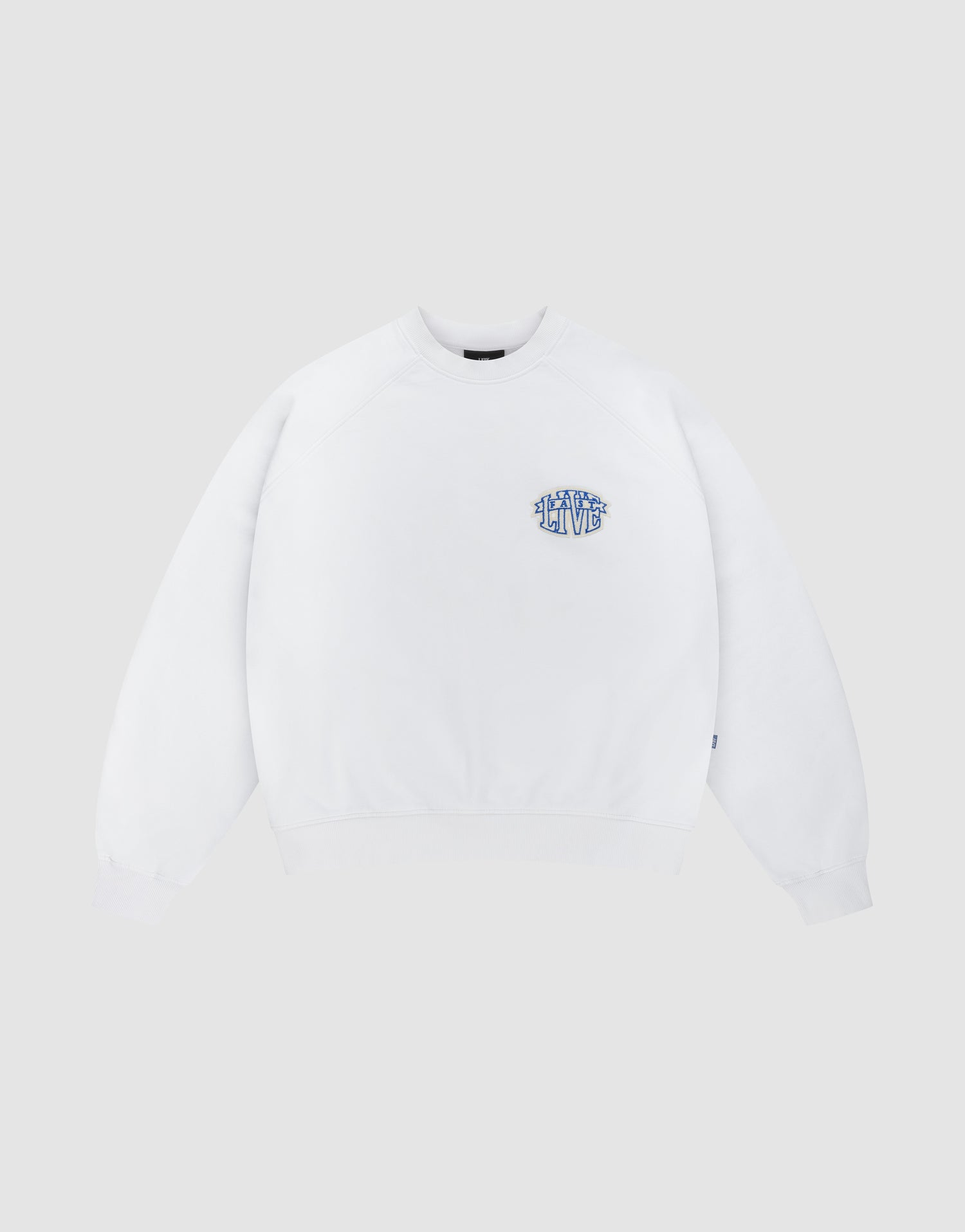 The LFDY Radiator Sweater by LIVE FAST DIE YOUNG is an oversized white crewneck featuring a small blue and yellow graphic text on the left chest, shown against a light grey background. | plain