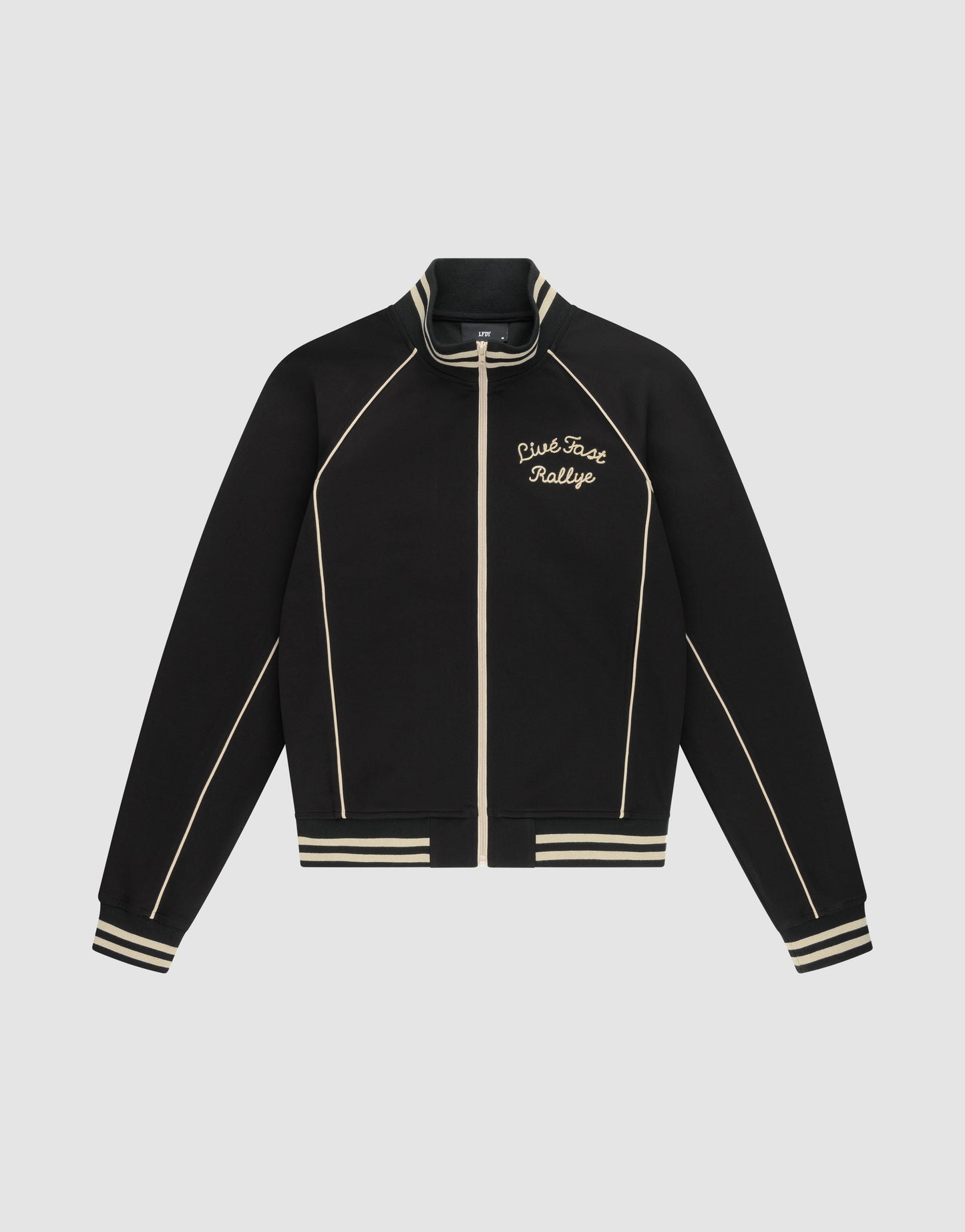 The Live Fast Tracksuit Jacket by LIVE FAST DIE YOUNG is a black jacket with cream piping, striped cuffs and hem, and a Chainstitch Live Fast Rallye logo on the left chest. Made from Baumwolle Polyester with a regular fit, it has a full zip and stand-up collar.