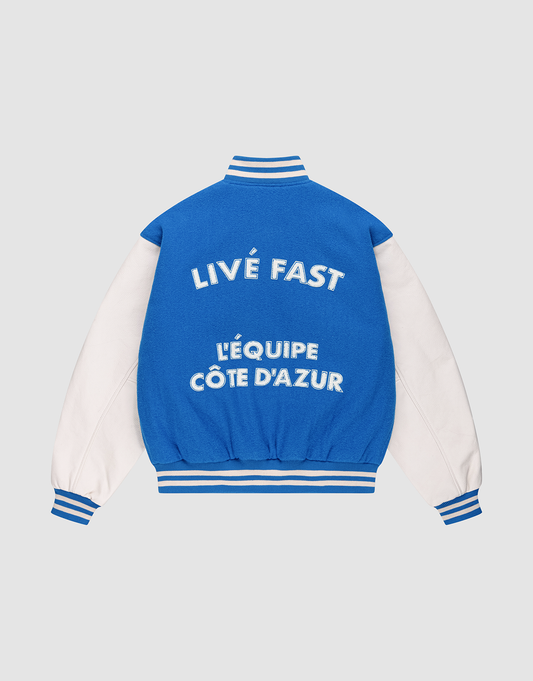 The LFDY x Schott NYC Varsity Jacket by LIVE FAST DIE YOUNG features blue and white colors, striped cuffs, collar, and hem. Bold text on the back reads LIVE FAST and LÉQUIPE CÔTE DAZUR on this limited edition piece with signature details.