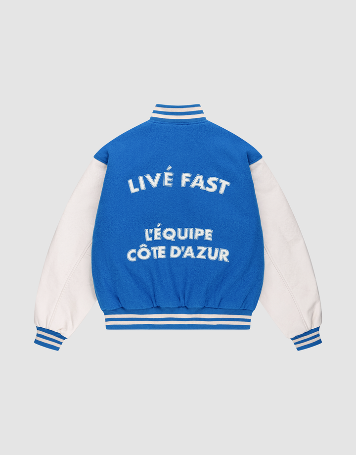 The LFDY x Schott NYC Varsity Jacket by LIVE FAST DIE YOUNG features blue and white colors, striped cuffs, collar, and hem. Bold text on the back reads LIVE FAST and LÉQUIPE CÔTE DAZUR on this limited edition piece with signature details.