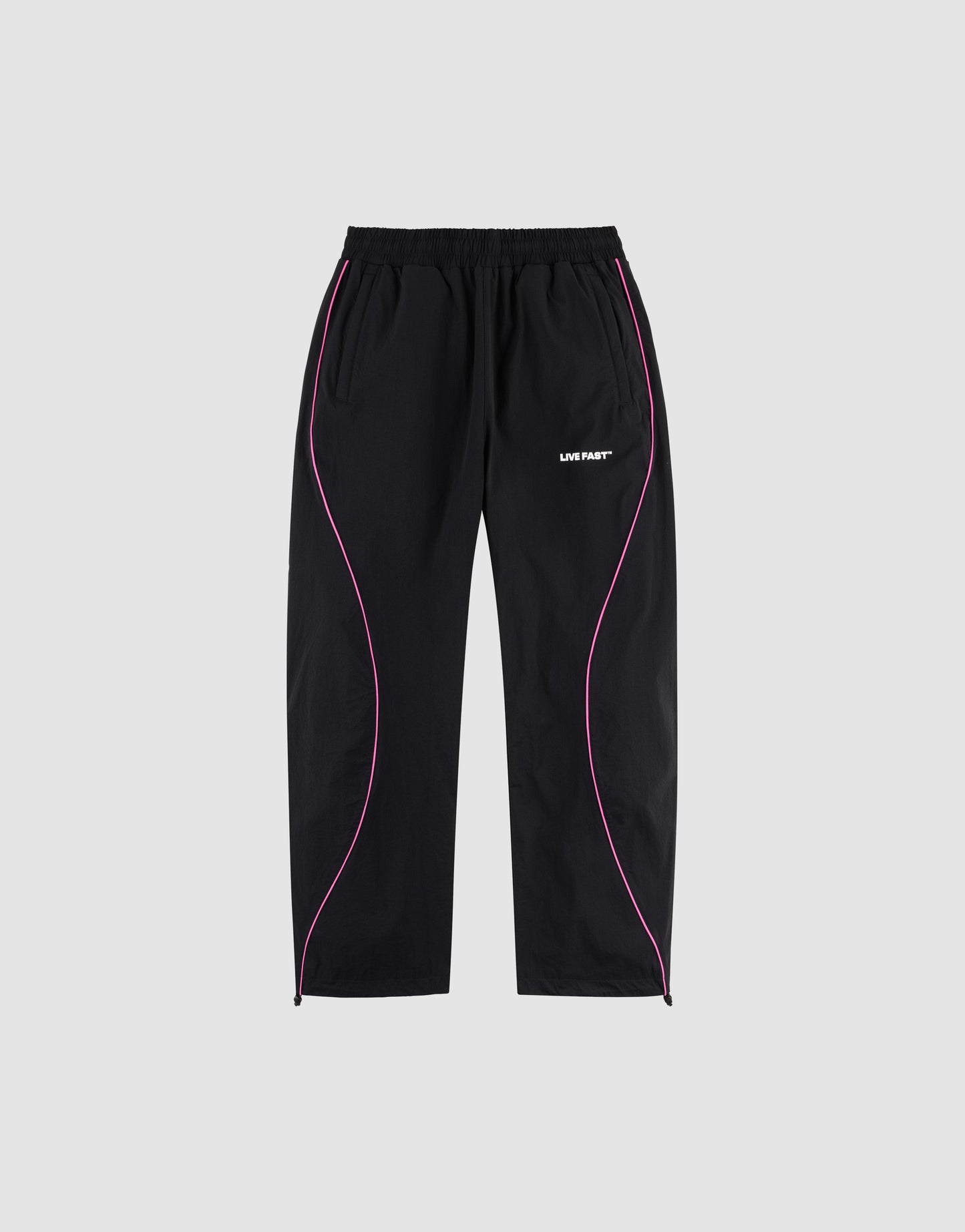 The LFDY Wavy Trackpants by LIVE FAST DIE YOUNG feature an elastic waistband, side pockets, wide fit, pink curved piping on black fabric, and a bold white "LIVIN FAST" logo print on the left thigh. Shown on a plain gray background.
