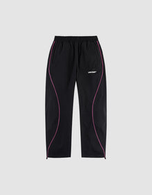 The LFDY Wavy Trackpants by LIVE FAST DIE YOUNG feature an elastic waistband, side pockets, wide fit, pink curved piping on black fabric, and a bold white "LIVIN FAST" logo print on the left thigh. Shown on a plain gray background. | plain