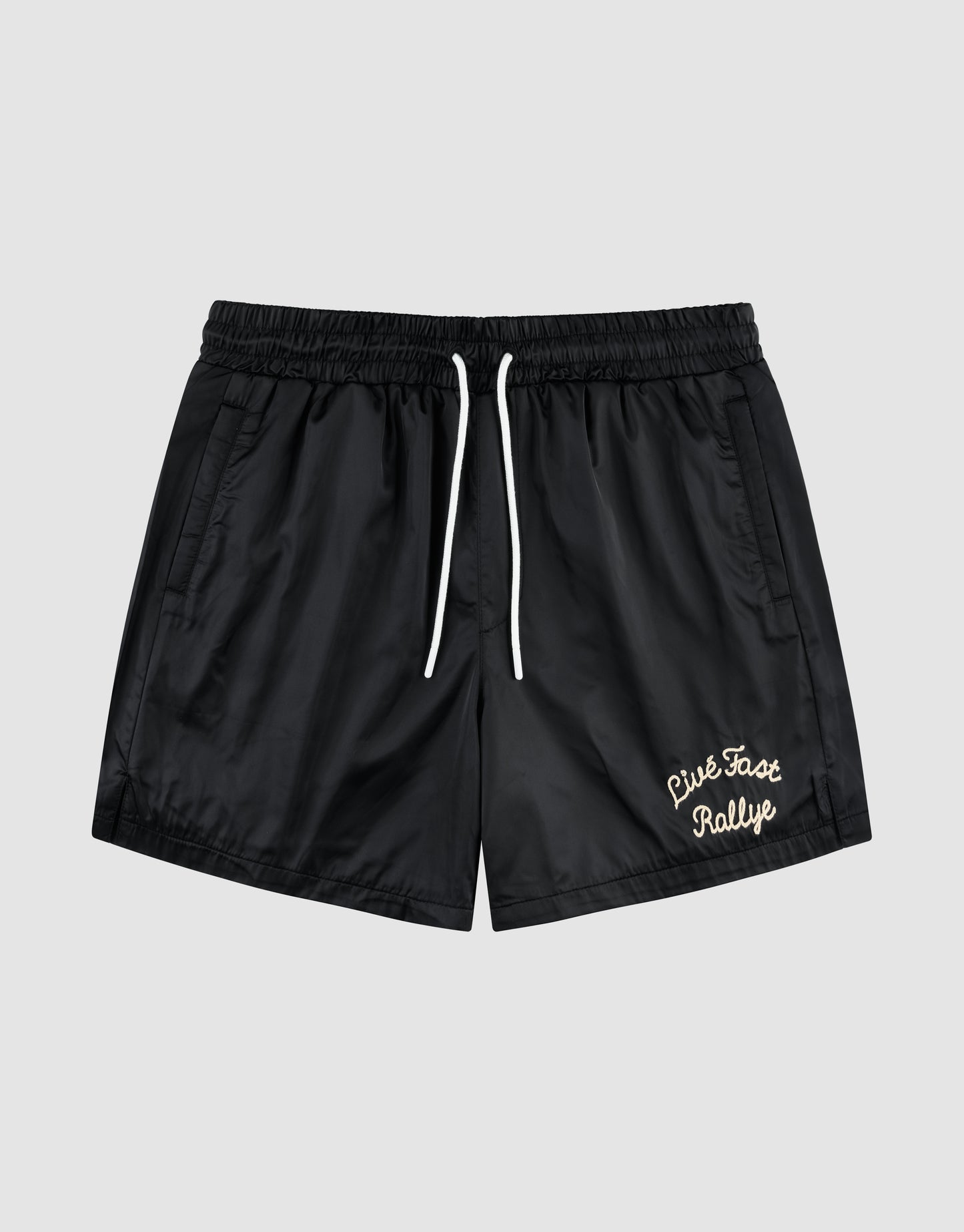 The LFDY Retro Satin Shorts by LIVE FAST DIE YOUNG feature a black design with white drawstrings, elastic waist, side pockets, and a white chainstitch "Live Fast Rallye" logo on the lower left leg, shown against a plain gray background.