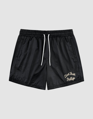 The LFDY Retro Satin Shorts by LIVE FAST DIE YOUNG feature a black design with white drawstrings, elastic waist, side pockets, and a white chainstitch "Live Fast Rallye" logo on the lower left leg, shown against a plain gray background. | plain