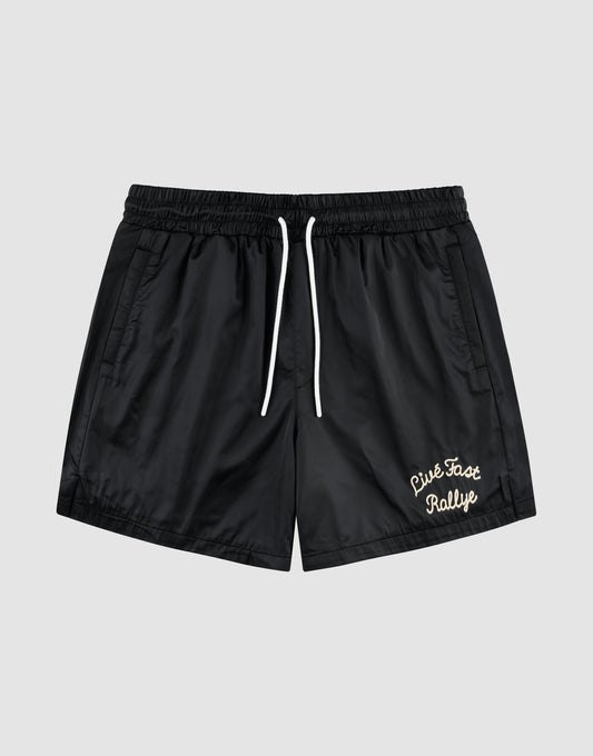 The LFDY Retro Satin Shorts by LIVE FAST DIE YOUNG feature a black design with white drawstrings, elastic waist, side pockets, and a white chainstitch "Live Fast Rallye" logo on the lower left leg, shown against a plain gray background. | plain