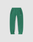 Basic Shell Pants by LIVE FAST DIE YOUNG: green track pants with elastic waistband and cuffs, black zippered side pockets, a white inner leg stripe, and small reflective "LVR FIRST" text on the left thigh, shown on a plain background.