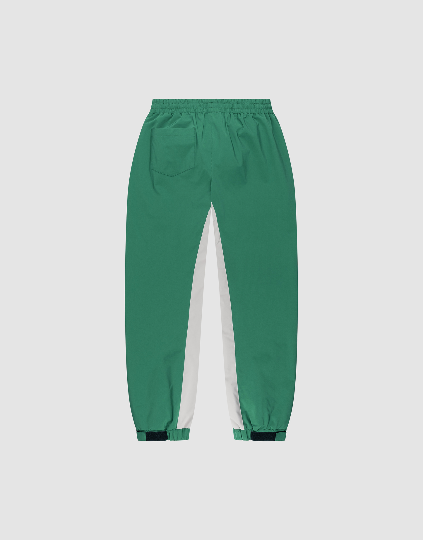 The LIVE FAST DIE YOUNG Basic Shell Pants feature a green color with white inner leg panels, elastic waistband, right back pocket, elastic cuffs, dark green adjustable ankle tabs, and an oversized fit. Displayed on a plain background.