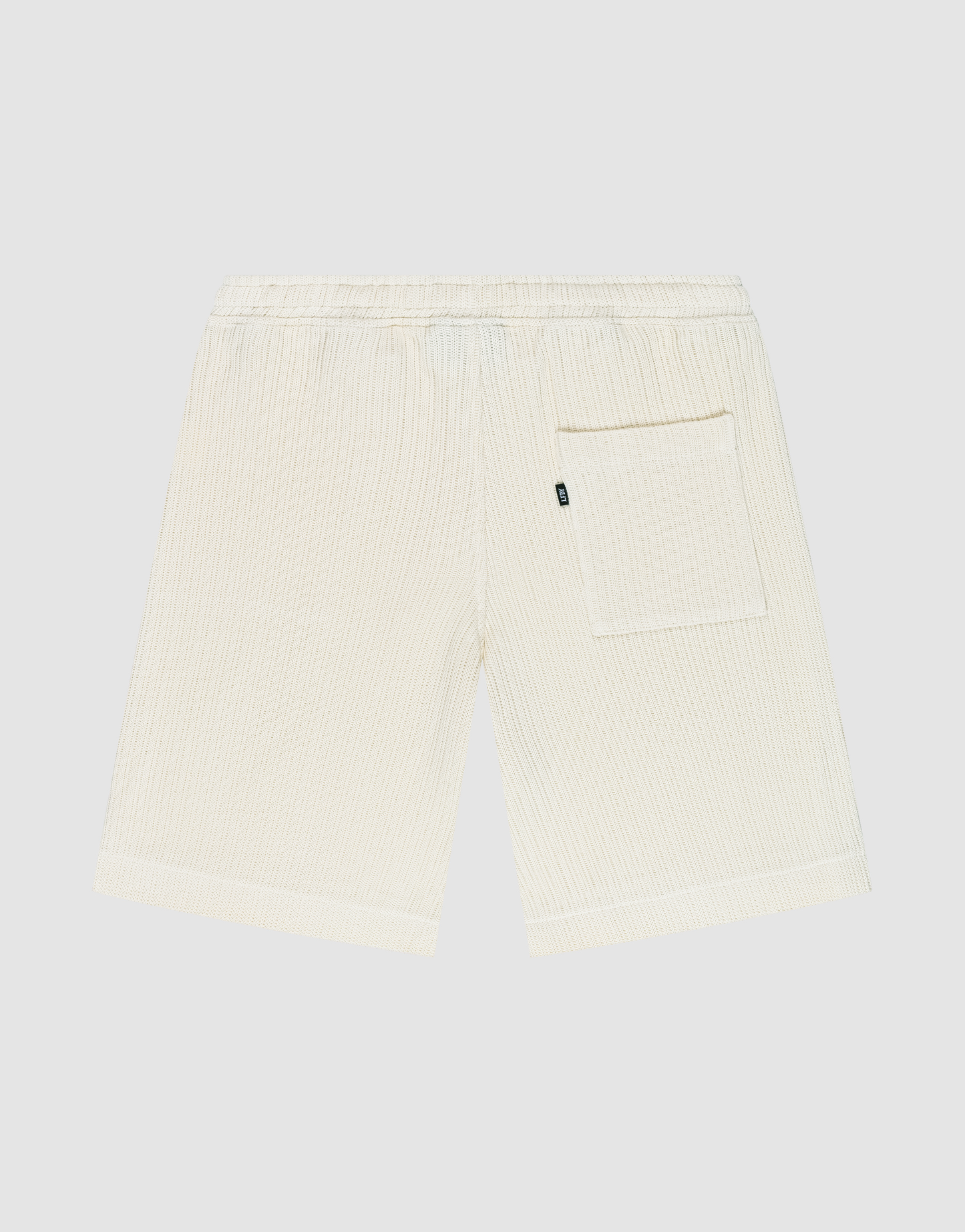 Back view of Basic Knit Shorts by LIVE FAST DIE YOUNG in cream, featuring subtle vertical stripes, elastic waistband, and a single right patch pocket. The shorts are displayed flat on a plain light background.