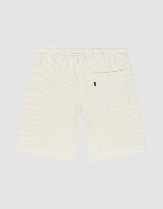 Back view of Basic Knit Shorts by LIVE FAST DIE YOUNG in cream, featuring subtle vertical stripes, elastic waistband, and a single right patch pocket. The shorts are displayed flat on a plain light background.