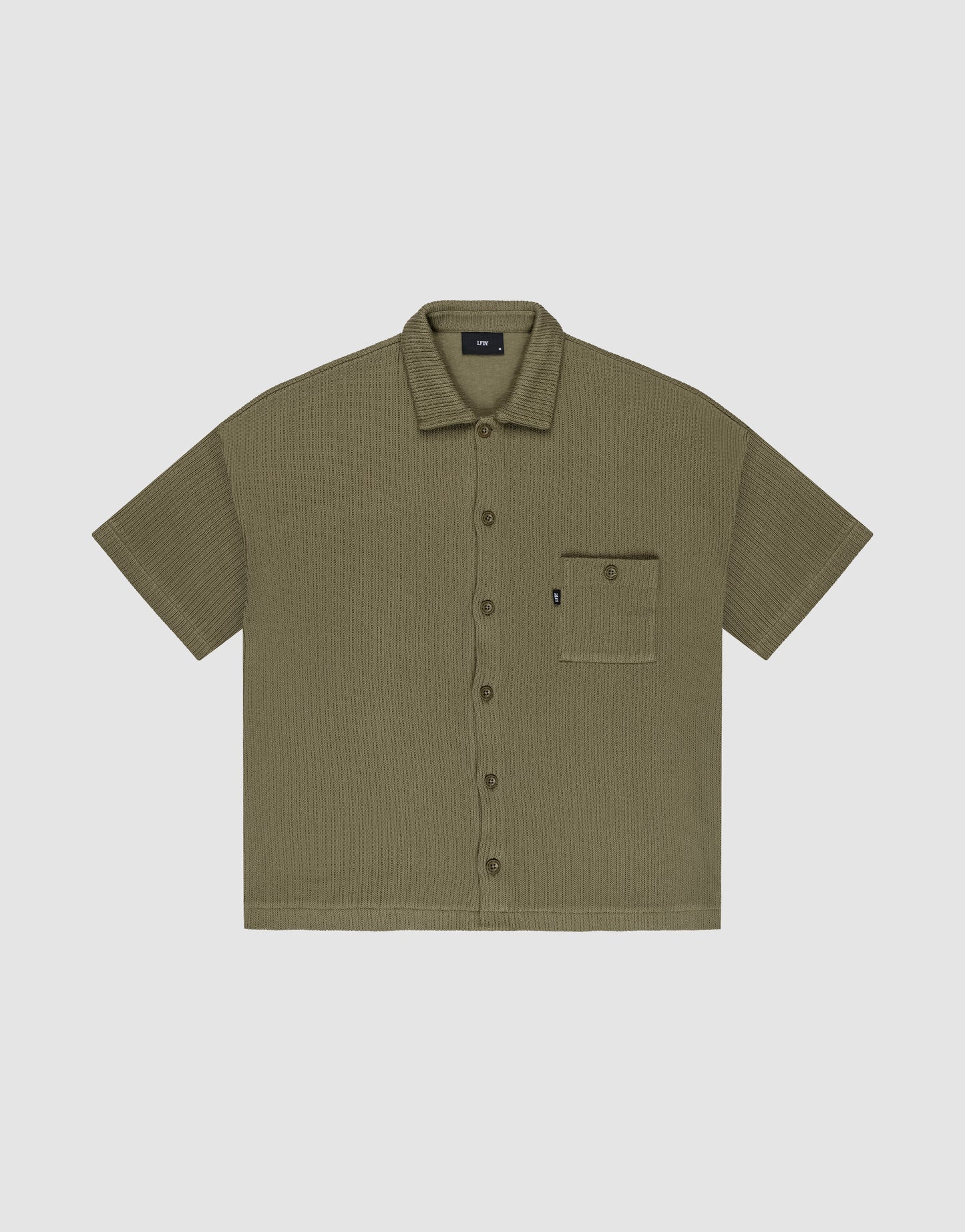 Olive green Basic Knit Shirt by LIVE FAST DIE YOUNG, oversize fit with short sleeves, textured fabric, and a single left chest pocket with a small black tag; shirt is laid flat on a light background.