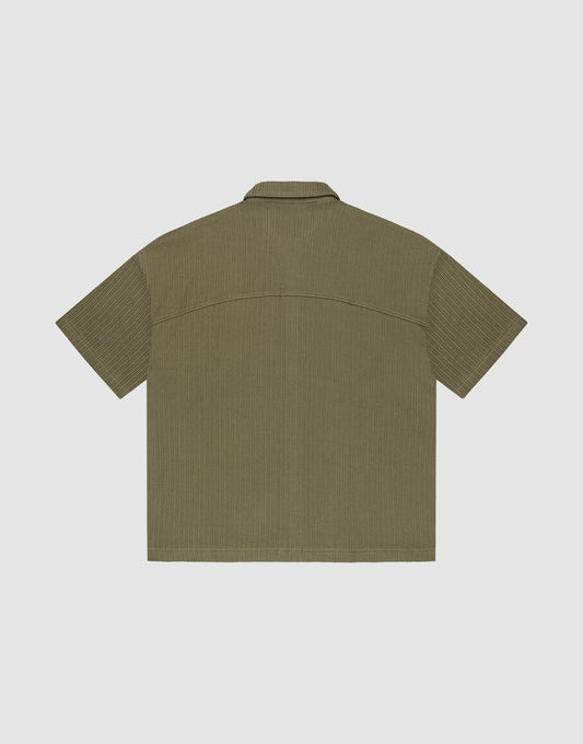 The LIVE FAST DIE YOUNG Basic Knit Shirt, shown flat from the back, is short-sleeved and olive-green with a subtle vertical texture, oversize fit, straight hem, and a simple collar.