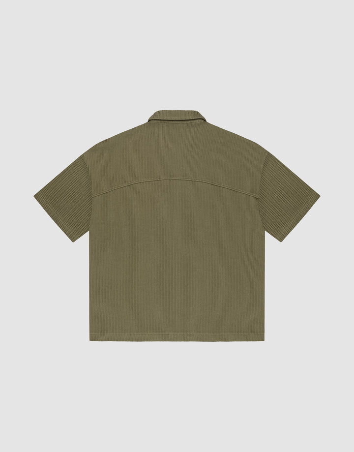 The LIVE FAST DIE YOUNG Basic Knit Shirt, shown flat from the back, is short-sleeved and olive-green with a subtle vertical texture, oversize fit, straight hem, and a simple collar.