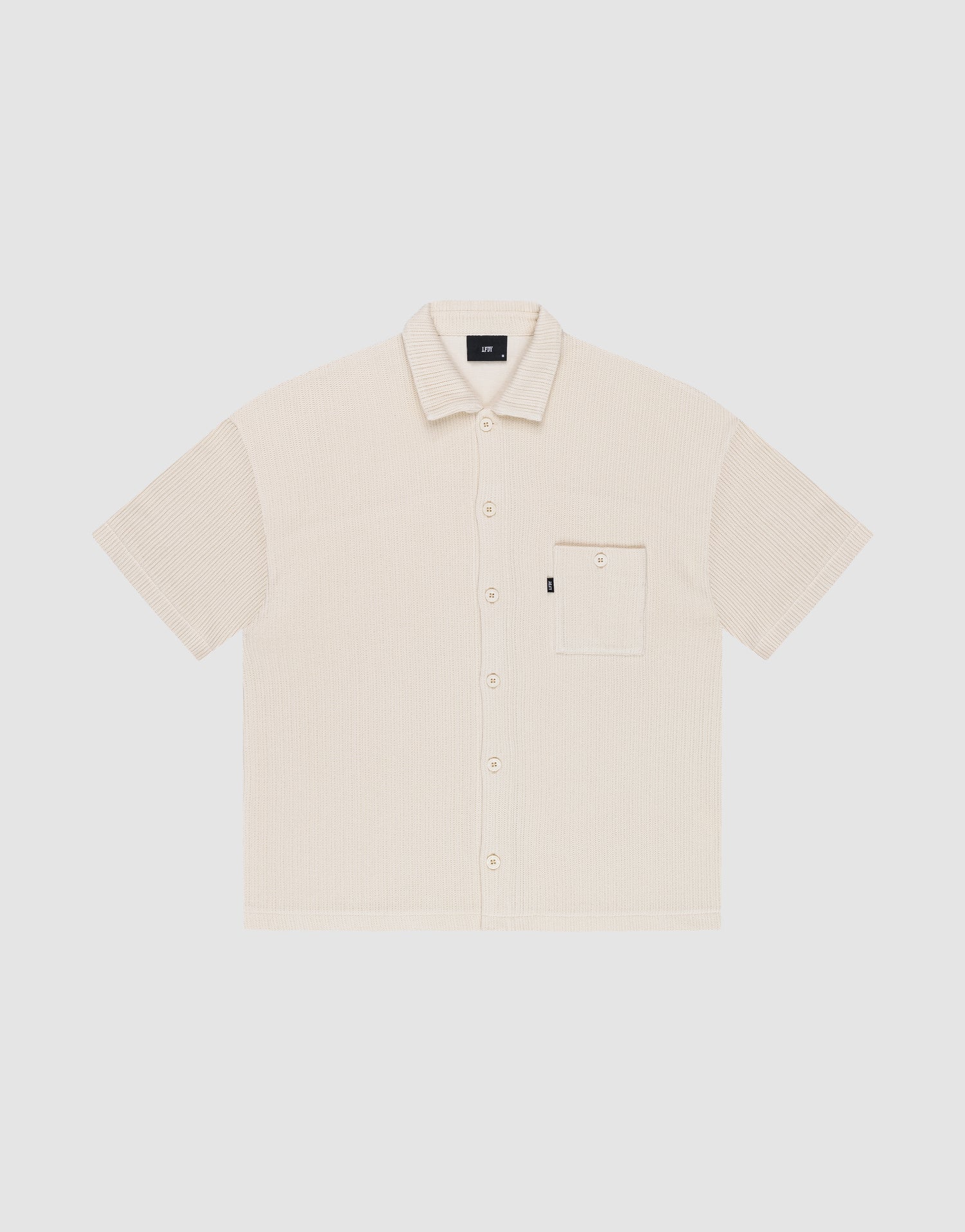 The Basic Knit Shirt by LIVE FAST DIE YOUNG is a short-sleeve, light beige button-up with a Hemdkragen, front chest pocket, and small black LFDY branding tag on the pocket, shown on a plain white background. | plain