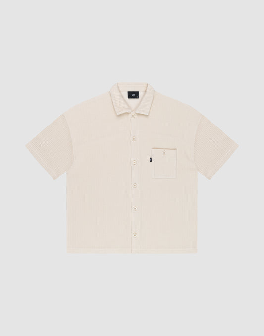 The Basic Knit Shirt by LIVE FAST DIE YOUNG is a short-sleeve, light beige button-up with a Hemdkragen, front chest pocket, and small black LFDY branding tag on the pocket, shown on a plain white background. | plain