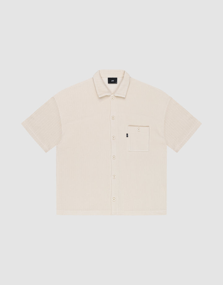 The Basic Knit Shirt by LIVE FAST DIE YOUNG is a short-sleeve, light beige button-up with a Hemdkragen, front chest pocket, and small black LFDY branding tag on the pocket, shown on a plain white background. | plain