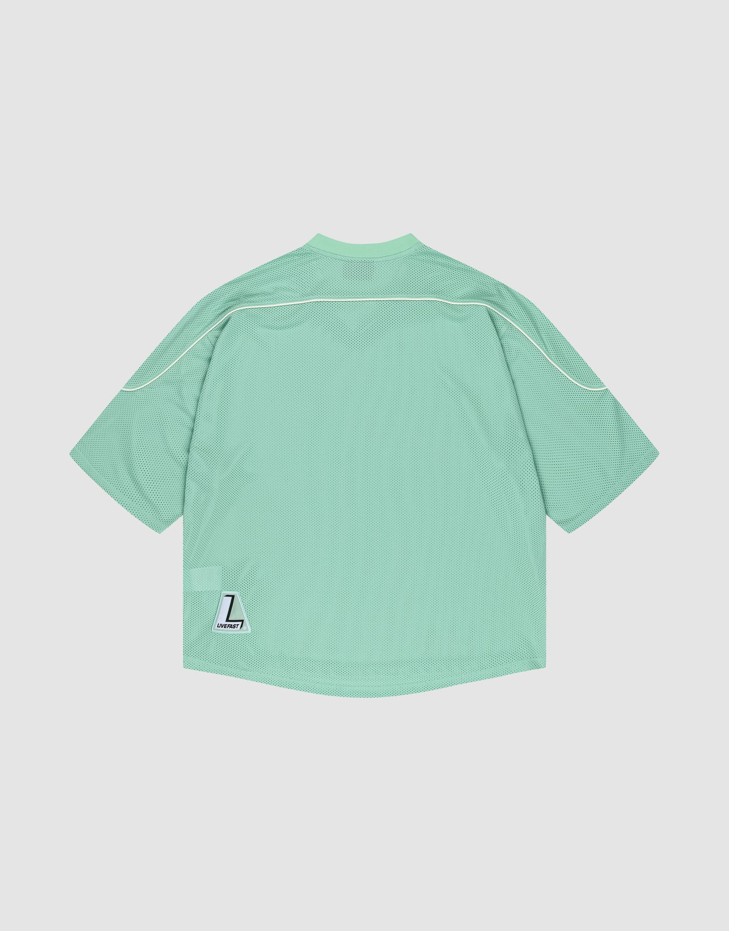 The LIVE FAST DIE YOUNG Basic Mesh Jersey is a mint green, oversized polyester sports top with white piping and a small white “L” Liberty patch near the lower left hem, shown against a plain white background.