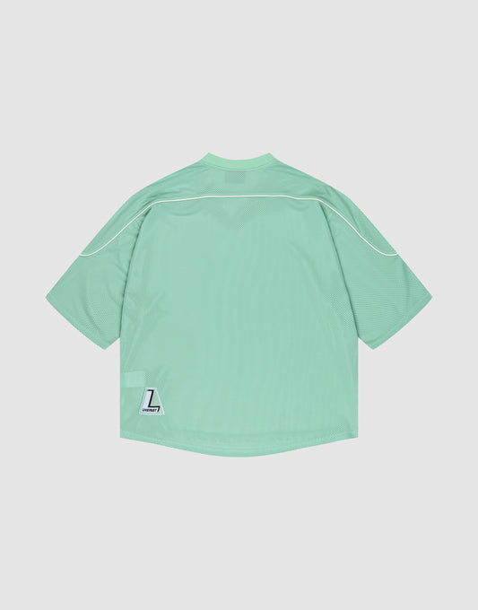 The LIVE FAST DIE YOUNG Basic Mesh Jersey is a mint green, oversized polyester sports top with white piping and a small white “L” Liberty patch near the lower left hem, shown against a plain white background.