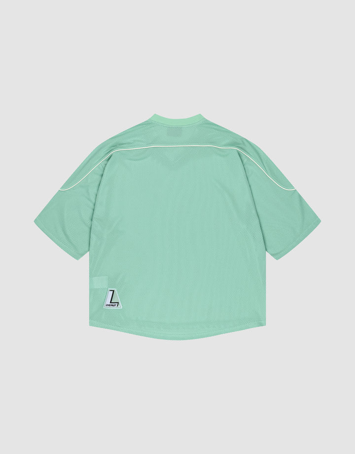 The LIVE FAST DIE YOUNG Basic Mesh Jersey is a mint green, oversized polyester sports top with white piping and a small white “L” Liberty patch near the lower left hem, shown against a plain white background.