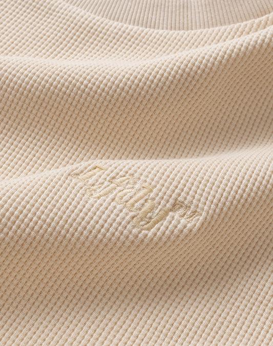 Close-up of the beige Basic Waffle Longsleeve by LIVE FAST DIE YOUNG, featuring ribbed knit fabric in cotton with subtle, slightly raised logo embroidery that adds soft texture and gentle shadows to the surface.
