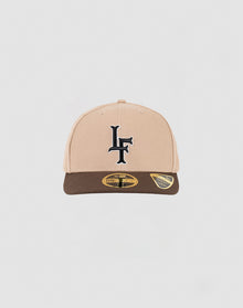 The LFDY x NEW ERA 59FIFTY Low Profile Fitted Cap by LIVE FAST DIE YOUNG features a beige and brown design, a black LF logo on the front, and two gold-and-black stickers on the brown brim, displayed against a white background.