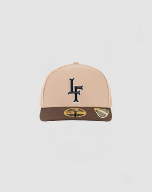 The LFDY x NEW ERA 59FIFTY Low Profile Fitted Cap by LIVE FAST DIE YOUNG features a beige and brown design, a black LF logo on the front, and two gold-and-black stickers on the brown brim, displayed against a white background.