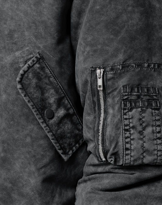 Close-up of the LIVE FAST DIE YOUNG Washed Bomber Jacket in black textured fabric, regular fit, featuring visible stitching, a vertical zipper pocket, and a flap with a black snap button.