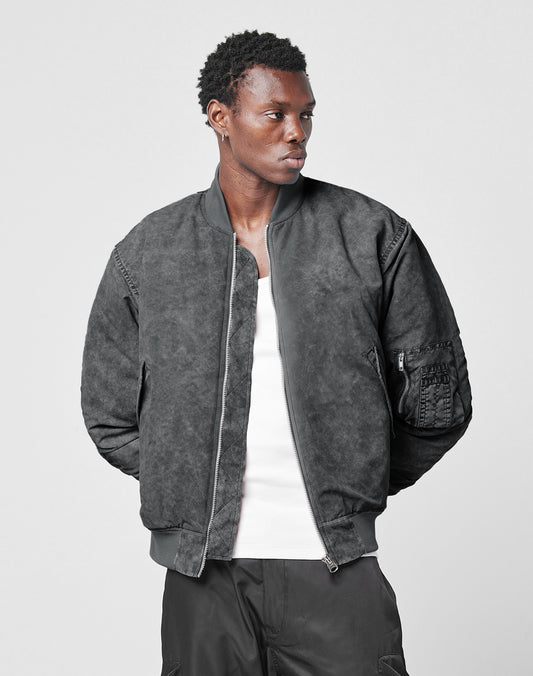 A young man models the LIVE FAST DIE YOUNG Washed Bomber Jacket in black, styled over a white tank top. He stands against a plain background, looking left with his hands behind his back.