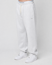 A person wears the LIVE FAST DIE YOUNG Basic Loose Jogger in light gray, featuring a logo print waistband with white drawstring, side pockets, and small embroidered detail on the left thigh, paired with white sneakers against a plain background.