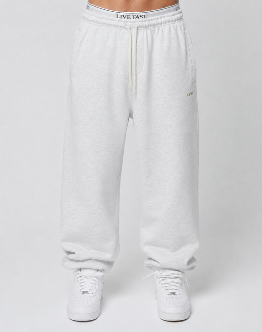 A person wears Basic Loose Jogger sweatpants by LIVE FAST DIE YOUNG with an elastic waistband and logo print, paired with white sneakers, standing against a plain light gray background. Only the lower body is visible.