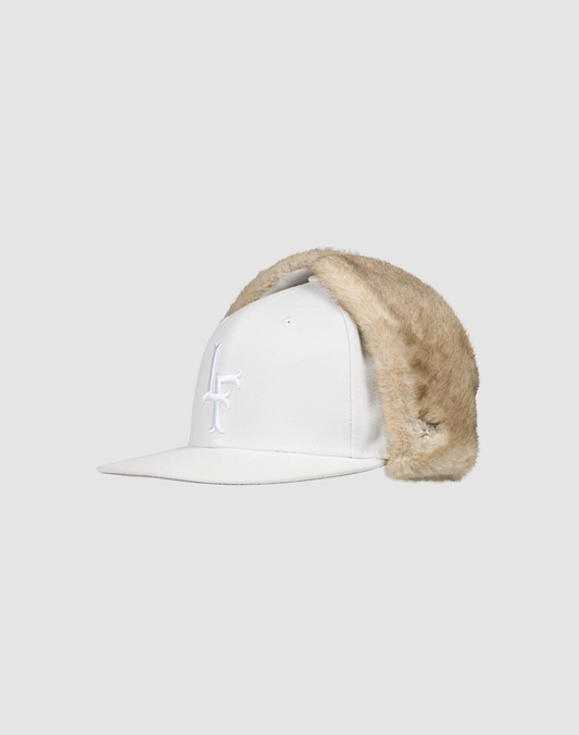 The LFDY x New Era 59Fifty DogEar by LIVE FAST DIE YOUNG is a white fitted cap with a light tan Kunstpelz earflap on one side and a white embroidered front logo, shown on a plain light gray background.