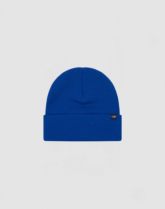 The LIVE FAST DIE YOUNG Basic Beanie is a plain royal blue polyacryl hat with a folded brim and a small black side flag label with white text, shown on a light gray background.