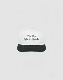 The LIVE FAST DIE YOUNG Live Fast Coffee Cap is a white, one size cap made from 100% Baumwolle with Live Fast Coffee & Cigarettes embroidered in dark green on the front, inspired by the LFDY Berlin Café and shown on a plain light gray background.