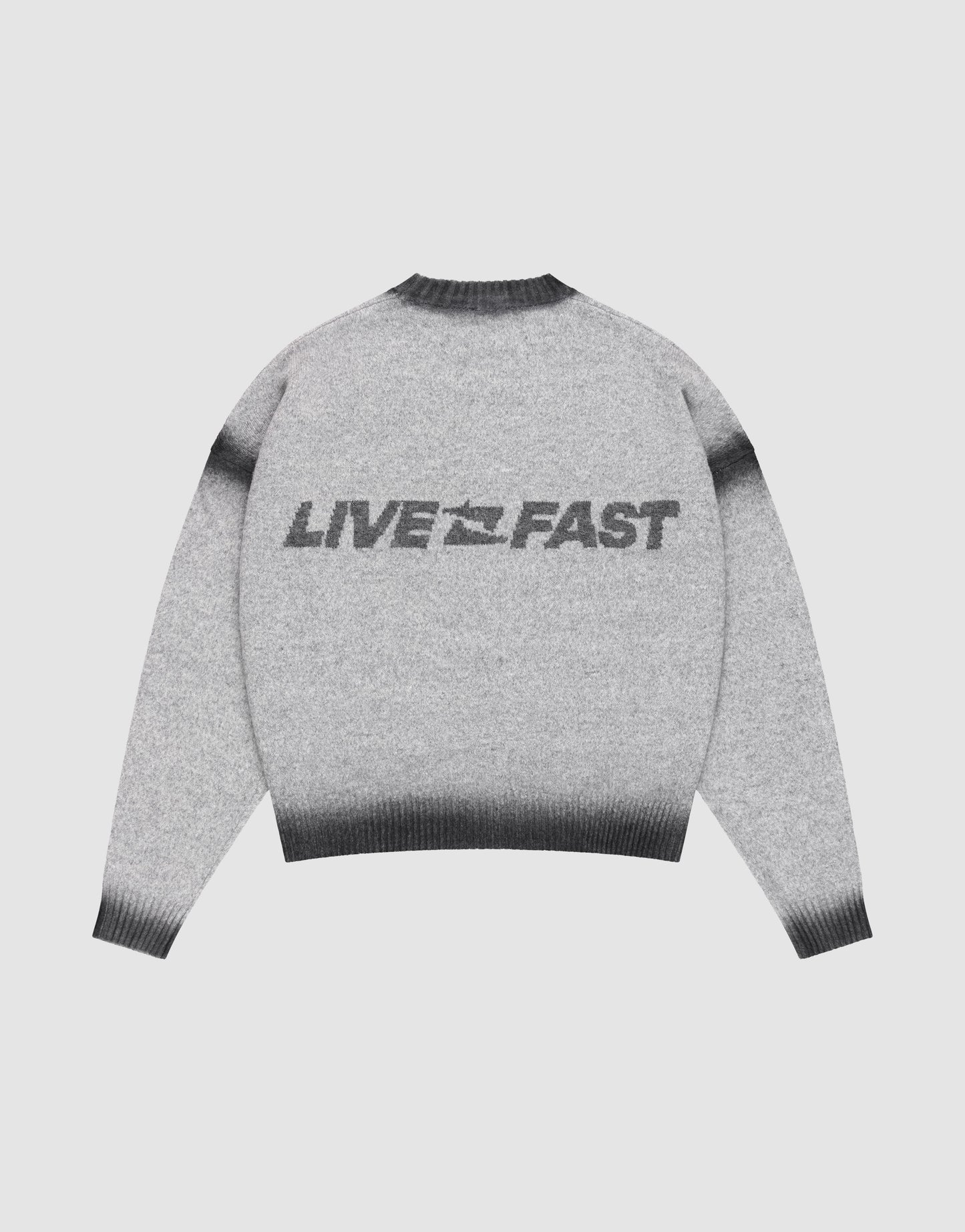 The LIVE FAST DIE YOUNG Live Fast Boucle Sweater features an oversize fit, gray tone, dark gradient cuffs, hem, and collar in a faded spray effect. "LIVE FAST" with a lightning bolt is printed bold on the back. Shown laid flat on a plain background.